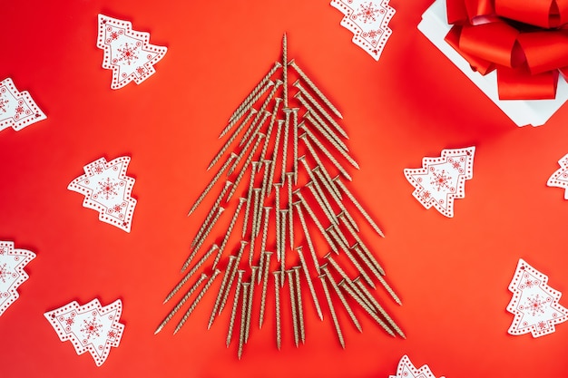 Self-tapping screws, laid out in shape of Christmas tree, wooden Christmas tree decorations, gift box on red background