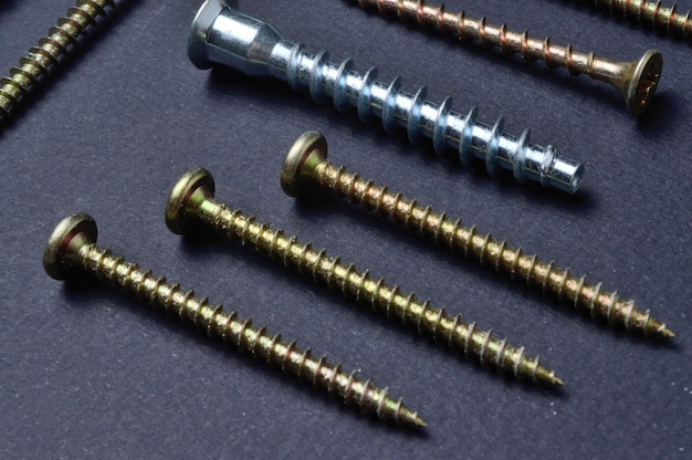 Self-tapping screws and various fittings are laid out on a dark surface