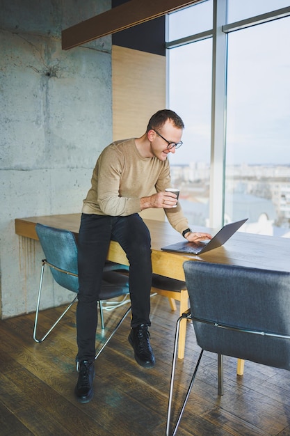 A selfemployed man in stylish clothes is making a blog website post on a laptop computer in a modern workspace Male freelancer works remotely and talks on the phone