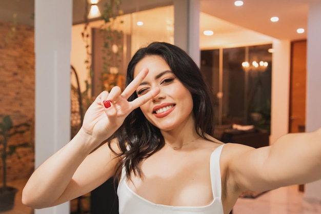 Selfie of a beautiful girl making the peace sign in the living room of her home