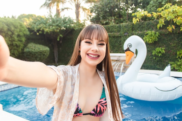 Selfie of a beautiful smiling girl in a bikini by the pool.