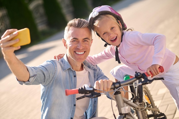 selfie. Een lachende man die selfie maakt met zijn kind op de fiets