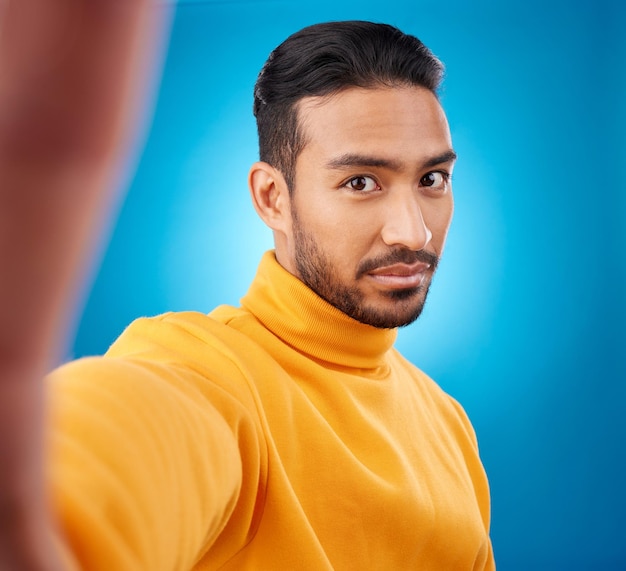 Photo selfie face and portrait of a young man in studio with hand style and fashion clothes serious male asian model on a blue background for social media platform or network profile picture update