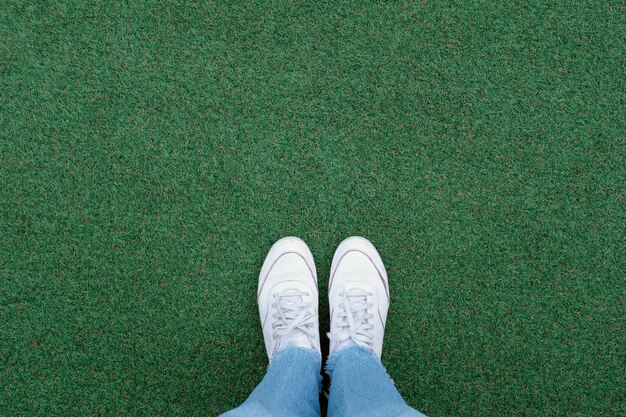 Selfie of feet in white sneakers shoes on green grass background with copy space, spring and summer with fashion lifestyle concept