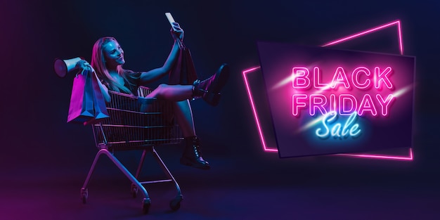 Photo selfie, megaphone. portrait of young woman in neon on dark studio backgound. human emotions, black friday, cyber monday, purchases, sales, finance concept. copyspace. seamless post for instagram.