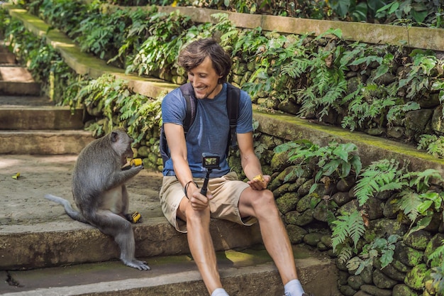 Selfie met apen. Jonge man gebruikt een selfiestick om een foto- of videoblog te maken met een schattige grappige aap. Reis selfie met dieren in het wild op Bali.