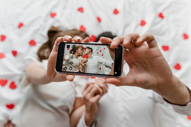 Selfie op telefoonscherm van man en vrouw verliefd in bed