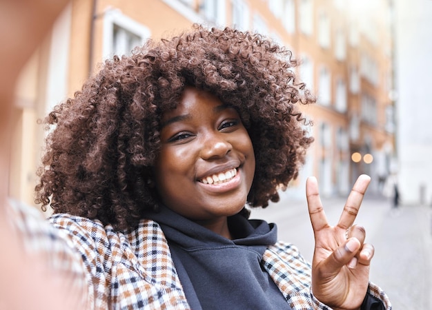 Selfie peace sign and black woman portrait with a smile from travel in a urban city Happy young person and face of a African female on a holiday with freedom by a building with blurred background