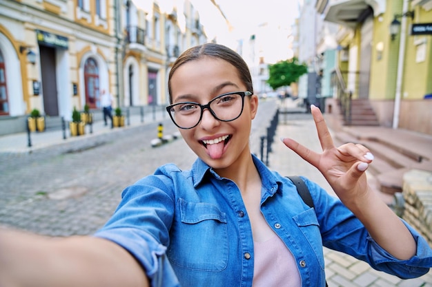 Selfie portrait of beautiful cheerful teenage girl outdoor on city street