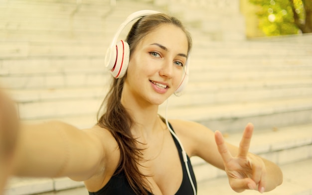 Selfie portrait of a cheerful sport woman in headphones. Healthy lifestyle. Gesture V