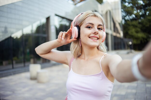 Photo selfie portrait of a cute young smiling girl with headphones in the city