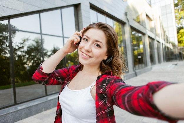 Selfie portrait of lovely woman listen music in headphones outdoors