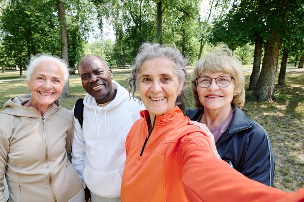 Photo selfie portrait of senior people in sportswear smiling at camera while standing outdoors