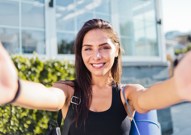 Selfie 초상화 야외에서 웃 고 그녀의 어깨에 가방 스포츠 정상에 젊은 쾌활 한 맞는 여자