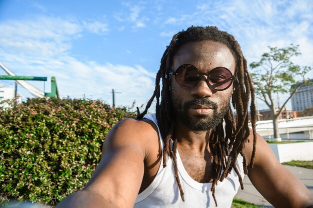 Selfie portret jonge Afrikaanse man met dreadlocks bril en baard kijkend naar de camera buiten