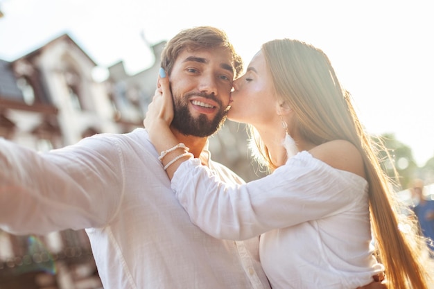 Foto selfie portret van een jong verliefd stel een mooi meisje kust haar vriend op de wang in de stad