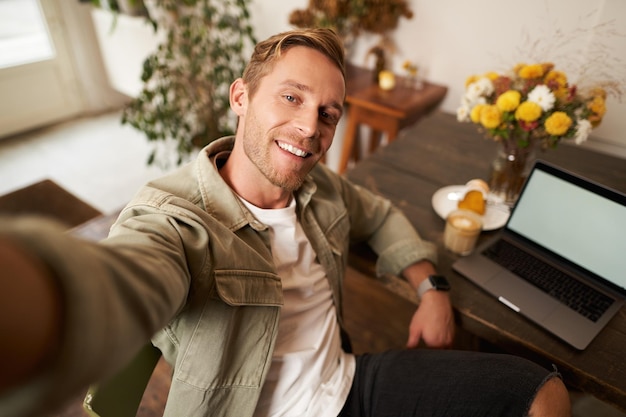 Selfie portret van een knappe jonge man die een foto van zichzelf maakt in een café met een laptop die naar hem glimlacht