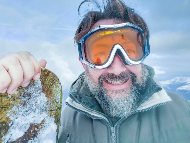 Selfie portret van oude volwassen man met snowboard alleen genieten van wintervakantie vakantie Jeugdige senioren in jonge sportactiviteiten Genieten van vrijetijdsbesteding in de buitenlucht in de bergen met sneeuw