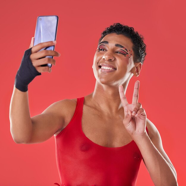 Selfie queer and gay man peace sign gesture for social media update isolated against a studio red background lgbtq non binary and gen z fashion model with online photo for the internet