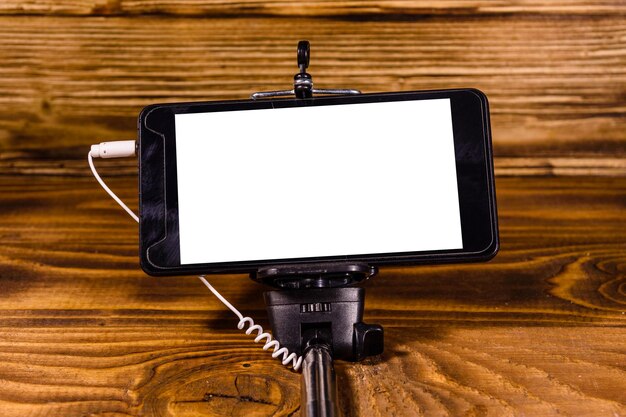 Selfie stick with modern smartphone on rustic wooden table