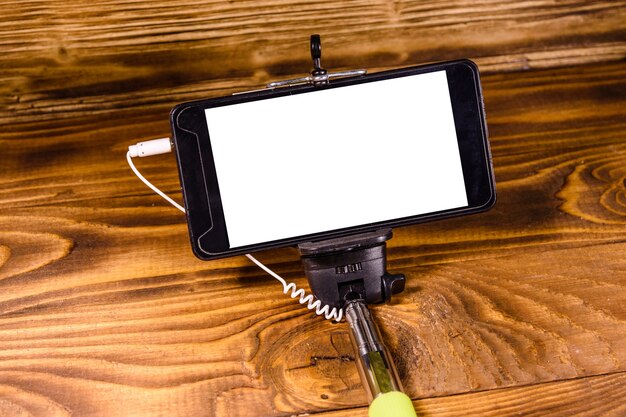 Selfie stick with modern smartphone on rustic wooden table