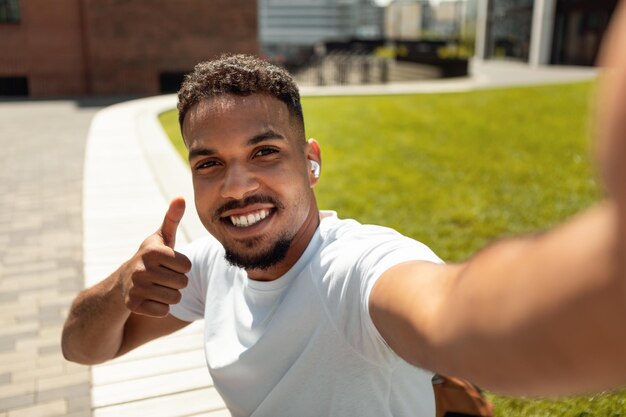 自分撮りの時間幸せなアフリカ系アメリカ人の男が彼の写真を作り、歩きながら親指を立てる