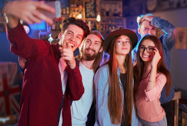 Фото Время селфи, молодая группа друзей, вечеринка в ночном клубе и поджаривание напитков счастливыми молодыми людьми