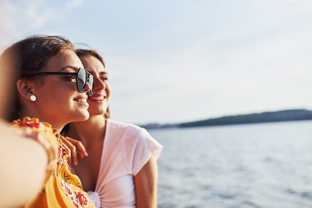 湖に対して晴れた日に一緒に良い週末を過ごす屋外の2人の笑顔の女の子の自分撮り。