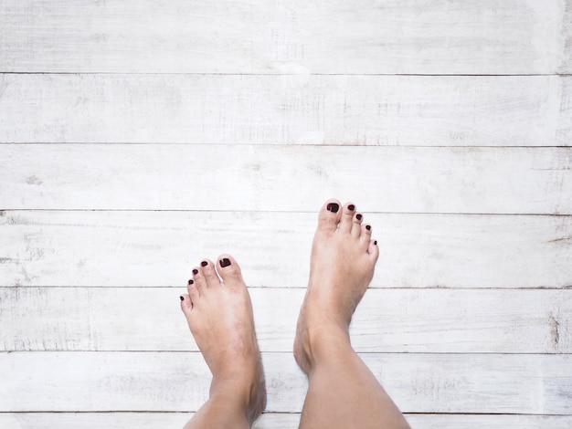 Photo selfie woman feet with dark red nails on white vintage wood white background.