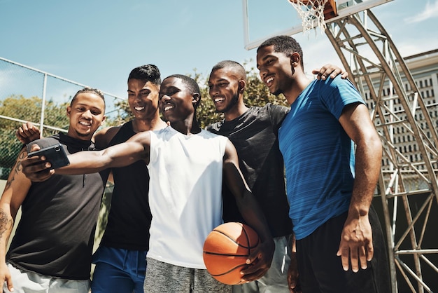 Selfiebasketbal en team op een sportveld voor partnerschapssamenwerking en training samen met een telefoon Gelukkige jongeren en atletengroep met een foto op smartphone terwijl ze fitnessoefeningen doen