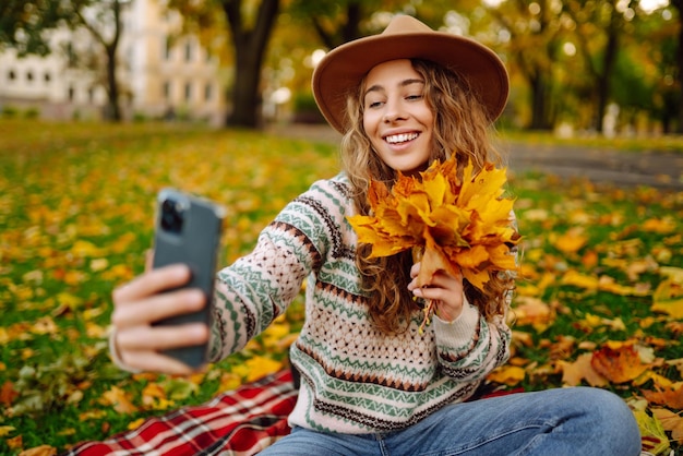 Selfietijd Mooie vrouw neemt selfie op smartphone in hoed op weide in herfstpark op plaid