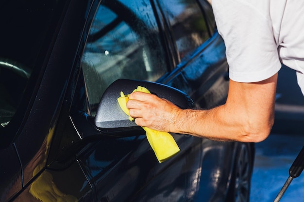 Selfservice carwash Een man veegt de spiegel van zijn auto schoon met een doek