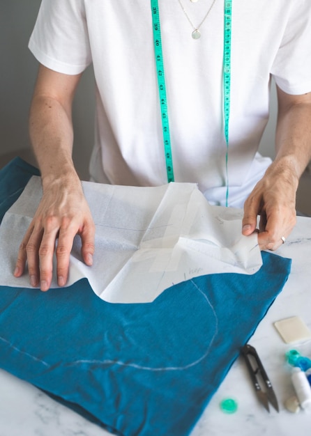 A selftaught seamster in white tshirt works with fabric pattern and chalk A male DIYdesigner transfers a template to fabric in a home studio Small business lifestyle concept