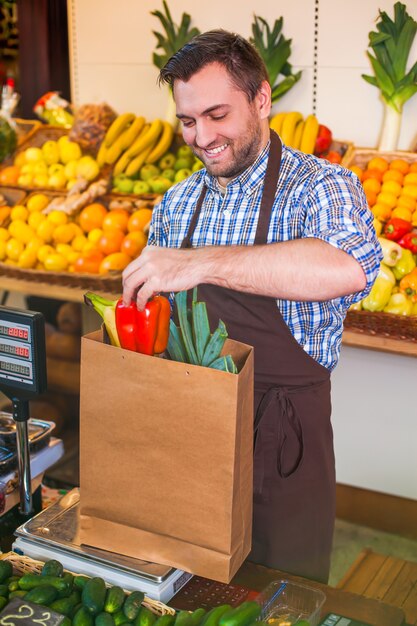 Продавец в фартуке складывает покупки в пакет.