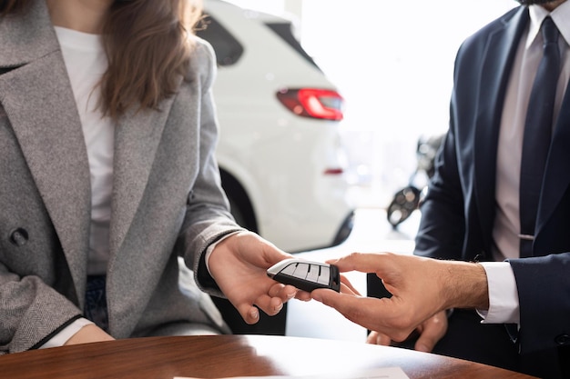 The seller in the car dealership gives the key to the new car to the buyer