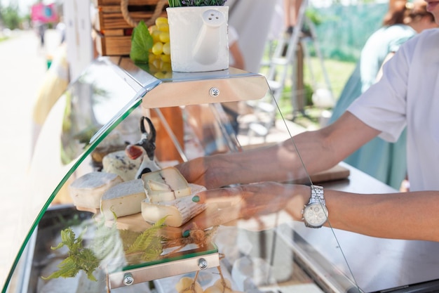 A seller in plastic gloves lays out homemade cheese on a glass counter at a street fair in the summer