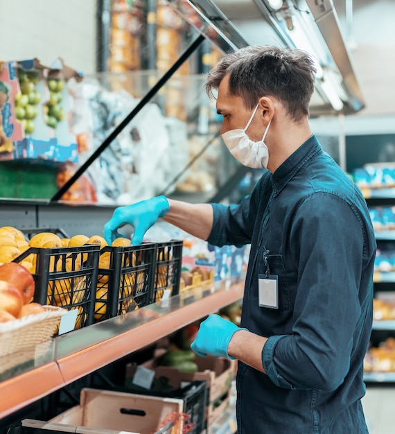 Photo seller in a protective mask standing in front of the counter with fruit. coronavirus in the city