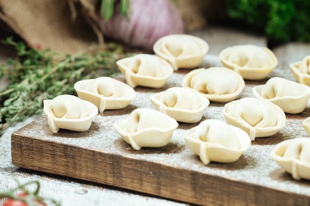 Semi-finished pelmeni dumplings on wooden board