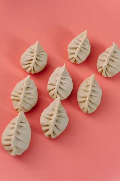 Semi-finished products on a pink surface. Top view of manti or dumplings. Pattern