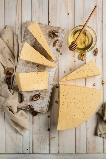 Photo semi-hard young cheese cut into pieces on a wooden board with honey. a great product for a morning breakfast. light wooden background. top view with a copy space for the text.