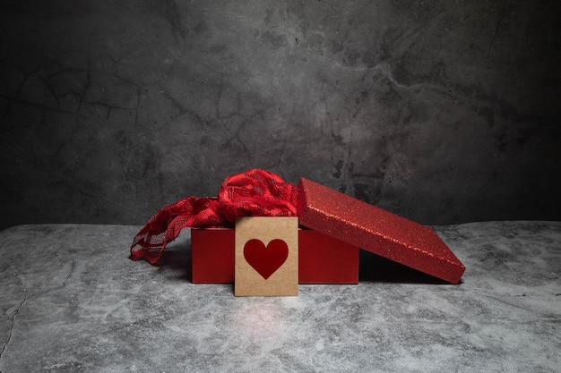 Полуоткрытая красная коробка с карточкой с сердечком перед коробкой на темном фоне