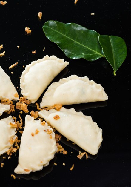 Semifinished dumplings mantas on a black background lying in a circle with onion and leafs