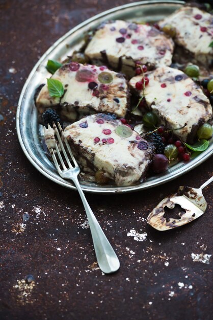 Semifreddo or italian cheese ice-cream dessert with garden berries and mint on vintage silver tray over metal rusty grunge background, top view.