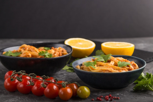 Semolina pasta with tomato pesto sauce, orange and herbs on a black concrete surface. Side view, selective focus, copy space.