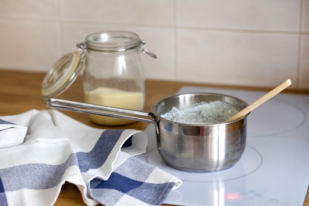 Porridge di semola in un mestolo di metallo su un fornello a induzione bianco preparazione della polenta di semola porridge in una casseruola