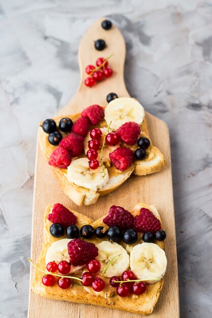 Sendvci with peanut butter, banana and raspberries and currants on a wooden board