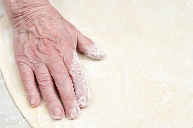 Seniele vrouwenhand bevlekt met bloem streelde het uitgerekte deeg, close-up