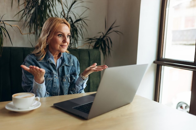 Senior 50s vrouw is online aan het werk bij caffe Ze zit voor een laptopmonitor en praat online videogesprek Concept Freelance