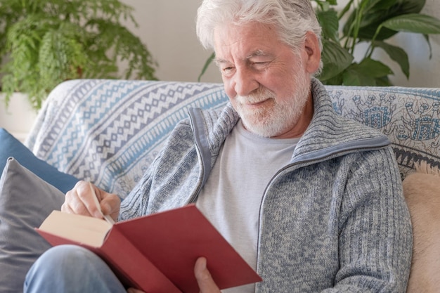 Photo senior 70s man seated on sofa leisure and people concept happy bearded senior man relaxing at home reading book