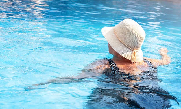 Senior active woman in a hat swims in the pool on vacation